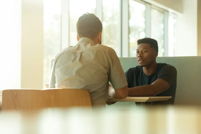 Deux personnes assises face à face autour d'une table, en pleine conversation dans un espace de travail lumineux.